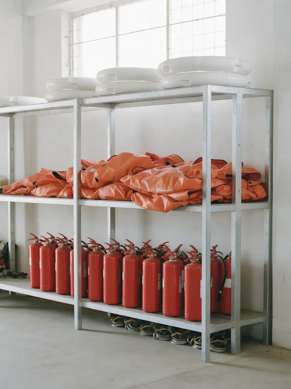 A liferaft canister, fire extinguishers and immersion suits on a rack.